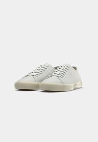 Adidași albi din pânză cu o talpă din cauciuc texturată, de culoare albă murdară. Au ochiuri metalice, șireți plata și un design minimalist.