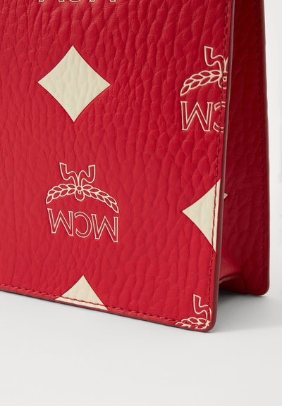 Red leather bag featuring an embossed diamond pattern and white accents. Displays a brand logo in a contrasting color at the top.