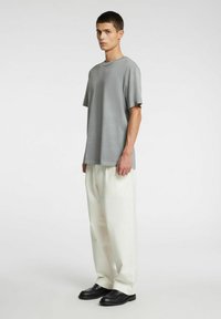 Szary t-shirt z krótkim rękawem o gładkiej fakturze, zestawiony z luźnymi białymi spodniami i czarnymi butami wsuwanymi.