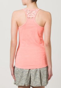 Koraal kleurige tanktop met een kanten achterkant, semi-aansluitende snit en een zachte textuur. Gecombineerd met een patroonrok in lichte en donkere kleuren.