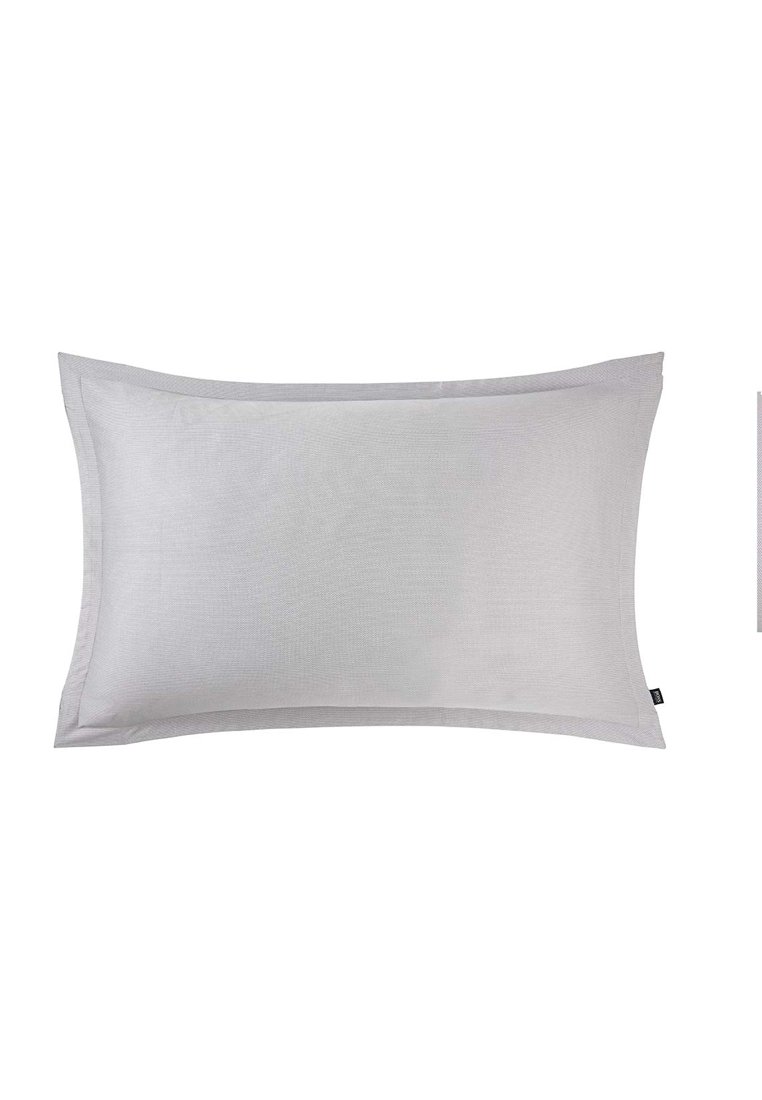 Coussin rectangulaire gris clair avec une surface en tissu texturé et une bordure cousue, comportant une petite étiquette sur un côté.