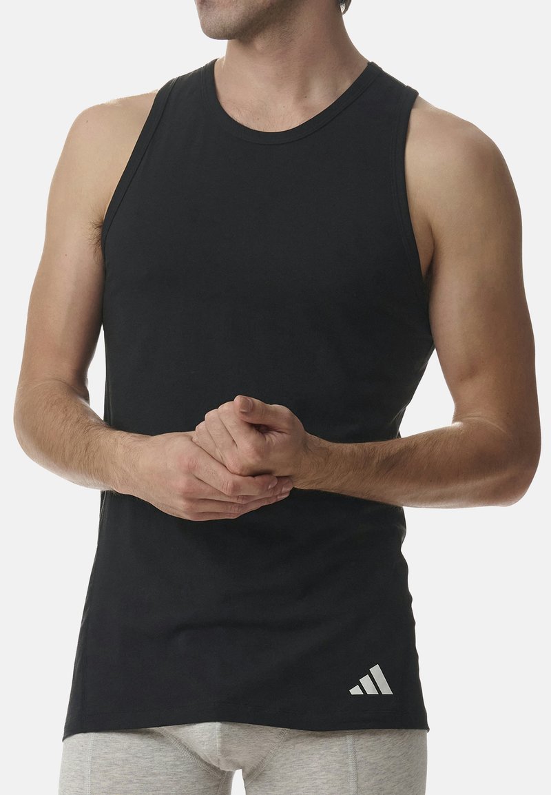 Svart linne i bomull med rund halsringning, ärmlös design och en vit Adidas-logotyp längst ner till höger.