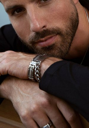 Close-up of hands wearing a silver chain bracelet and a metal link bracelet. Smooth texture, metallic sheen, and distinct designs are visible.