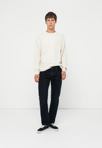 Lichtbeige geribde trui, donkerblauwe jeans, zwarte sneakers. Eenvoudige, casual outfit met contrasterende kleuren en een ontspannen pasvorm.