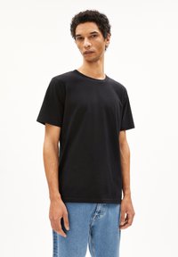 Schwarzes Baumwoll-T-Shirt mit kurzen Ärmeln und Rundhalsausschnitt. Der Stoff hat eine glatte Textur und ein minimales Design. Kombiniert mit hellblauen Jeans.