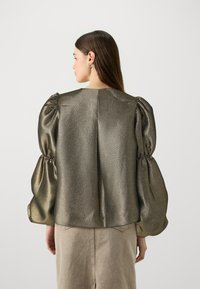 Blusa dorata metallica con tessuto strutturato, caratterizzata da maniche a sbuffo voluminose e scollatura rotonda semplice. Finitura liscia con motivo geometrico.