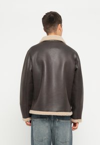 Bruine leren jacket met een schapenvacht kraag en zoom; heeft een gladde textuur en een ontspannen pasvorm. Lichte accenten bij de manchetten en zoom.