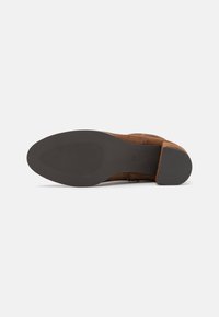 Stivale alla caviglia in suede marrone con suola in gomma nera liscia, caratterizzato da un tacco leggermente affusolato e rigature orizzontali per una migliore aderenza. Taglia 37.