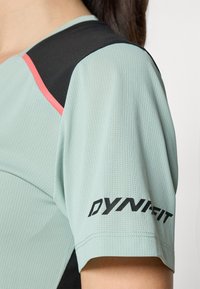 Mintgrønn treningsskjorte med svarte og korallfargede detaljer. Har strukturert stoff og "DYNAFIT"-logo på ermet.