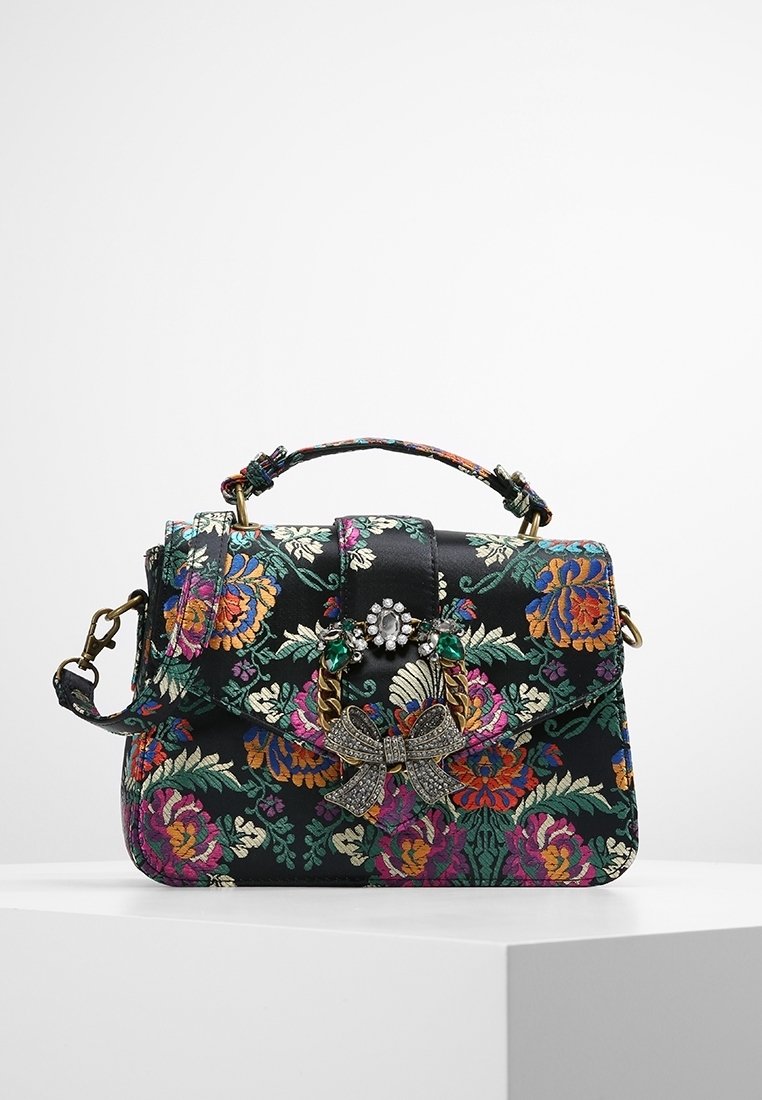 Czarna torebka w kwiaty z kolorowym haftem, złotymi akcentami, dekoracyjną kokardą oraz zapięciem ozdobionym klejnotami. Kompaktowy prostokątny kształt.