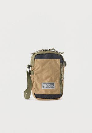 Συμπαγής θήκη Fjällräven σε χρώματα μαυριδά και ελιά με μπροστινή τσέπη με φερμουάρ, λογότυπο και προσαρτημένο λουράκι καρπού σε ανοιχτό φόντο.