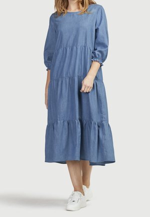 Denim midi kjole med lagdeling, rund halsudskæring, pufærmer, samlede sømme og en flydende silhuet. Sammen med hvide sneakers.