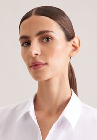 Weißes Hemd mit Kragen und glatter Textur, das ein klassisches Design aufweist. Nahaufnahme eines Gesichts mit glattem Haar und sanft beleuchteter Haut.