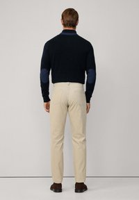 Pull marine foncé avec des coudières, pantalon beige et bottes marron. Tissu lisse avec un design ajusté et un détail de col contrasté.
