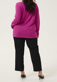 Fuchsia långärmad topp med en avslappnad passform, i kombination med svarta raka byxor. Modellen bär svarta sandaler med öppen tå.