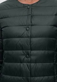 Gros plan d’une veste matelassée noire avec des coutures horizontales et des boutons-pression ronds noirs le long de la fermeture avant.
