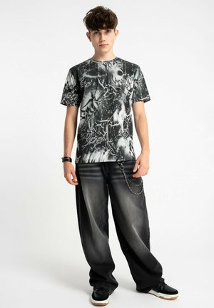 Czarny i biały t-shirt w abstrakcyjny wzór z okrągłym dekoltem, w połączeniu z luźnymi, wyblakłymi czarnymi dżinsami z akcentem w postaci łańcucha.