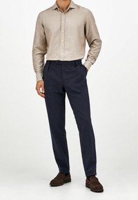 Camicia beige chiaro con bottoni e finitura strutturata, abbinata a pantaloni sartoriali blu scuro e mocassini in camoscio marrone.