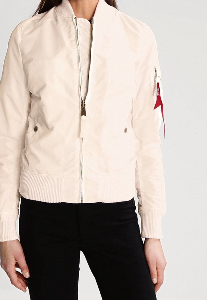 Veste bomber rose clair en nylon lisse avec fermeture éclair à l'avant, poignets côtelés et poches latérales. Présente un accent rouge sur la manche.
