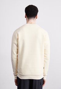 Sweatshirt crem deschis, dintr-un material moale, cu guler rotund, manșete ribbate și un tiv dreapt. Dispune de un etichetă pe partea stângă jos.