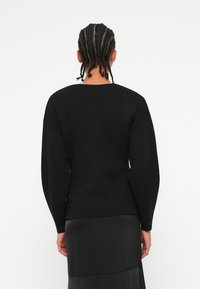 Černý pletený svetr s kulatým výstřihem, dlouhými nabíranými rukávy a úzkým střihem. Látka má hladkou strukturu.