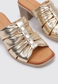 Sandalias de deslizamiento con tacón bloque metálico dorado que presentan tres tiras recogidas, una suela lisa y un diseño de punta redondeada.