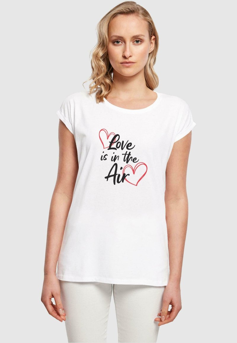Balta trumpa rankovė t-shirt maikutė, dekoruota spauda su tekstu "Meilė yra ore" juoda ir raudona spalva, su širdelėmis.