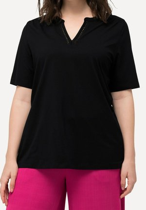 Kobieta w czarnym topie z krótkim rękawem i dekoltem w serek z koronkową lamówką, zestawionym z jaskraworóżowymi spodniami, pokazana od ramion do bioder.