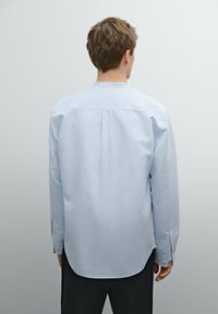 Camicia azzurro chiaro a maniche lunghe con taglio dritto, polsini abbottonati e una piega posteriore. Tessuto morbido con colletto classico e orlo arrotondato.