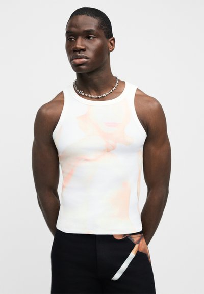 Λευκή αμάνικη φανέλα με αφηρημένο, παστέλ σχέδιο. Εφαρμοστή γραμμή και ομαλή υφή. Φοράται με μαύρο παντελόνι που έχει σχέδιο στην τσέπη.