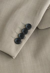 Manche de costume beige texturé avec quatre boutons noirs à quatre trous cousus verticalement près de la couture du poignet.