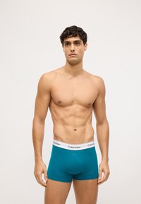 Miękkie, zielone bawełniane bokserki z białym paskiem z logo Calvin Klein. Materiał jest gładki, odpowiednio dopasowany, z minimalną ilością szwów i bez dodatkowych wzorów.