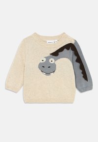 Texturerad beige stickad tröja med ett grått tecknat karaktärs ansikte och svarta detaljer på ärmen. Har rund halsringning och knappdekoration.