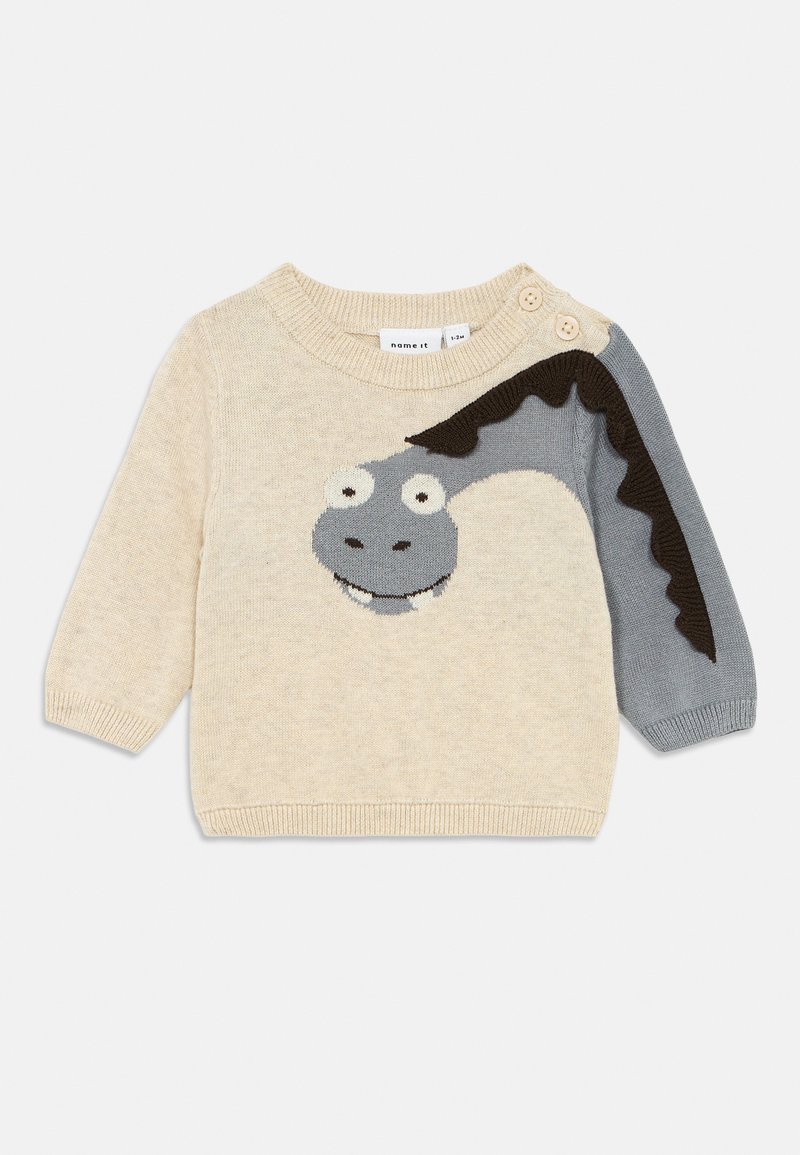 Maglione beige a maglia con texture, dotato di un volto di personaggio dei cartoni animati grigio e dettagli neri sulle maniche. Presenta un collo rotondo e bottoni decorativi.