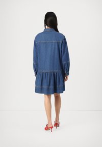 Jeanskjole med puffede langærmer, lagdelt kant og synlig syning. Et par røde højhælede sko er også synlige.