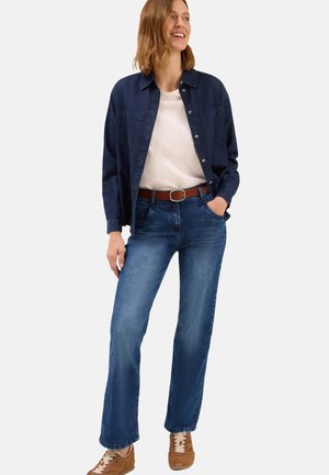 Jeans en denim bleu avec une coupe droite, associés à un t-shirt blanc et une chemise boutonnée bleu foncé, complétés par une ceinture marron et des baskets beiges.