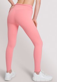 Roze high-waisted leggings gemaakt van rekbare stof. Heeft een gladde textuur en een aansluitend ontwerp, gecombineerd met witte sport sneakers.
