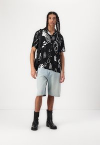 Svart kortermet skjorte med hvite abstrakte mønstre, kombinert med lyseblå denimshorts og svarte ankelstøvler. Enkelt design med en avslappet passform.