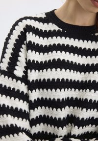 Maglione lavorato a maglia bianco e nero con strisce zigzag orizzontali, superficie testurizzata e scollatura a girocollo.