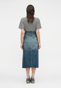 Μίντι τζιν φούστα σε διαβαθμισμένο μπλε χρώμ α με πίσω τσέπες και θηλιές για ζώνη, συνδυασμένη με μαύρο και άσπρο ριγέ μπλουζάκι και γκρι αθλητικά παπούτσια.