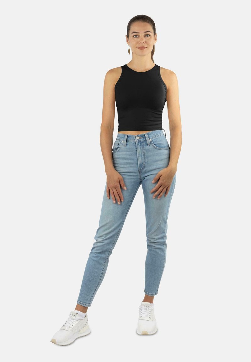 Schwarzes, kurzes Tanktop, hellblaue, hochgeschnittene Jeans und weiße Sneaker. Einfaches, figurbetontes Design mit glatter Textur und klassischen Akzenten.