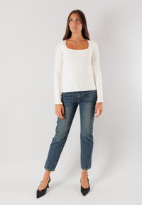 Top a maniche lunghe bianco a coste con scollo quadrato, abbinato a jeans in denim blu chiaro e décolleté nere a punta.