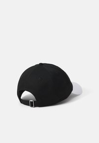 Sort kasket med en hvid skygge, stofstruktur, justerbar rem bagpå, samt en rund krone med syninger og ventilationshuller.