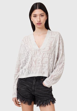 Pull en tricot gris clair avec un col en V, présentant un motif texturé. Associé à un short noir avec un ourlet effiloché.