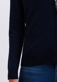 Marinblå zip-up kofta i mjukt stickat tyg, med ribbade ärmslut och fåll, samt en sidoficka på vänster sida.