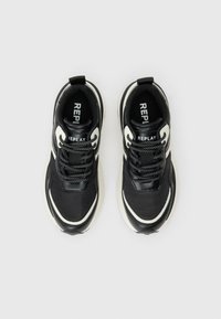 Par črno-bele superge blagovne znamke Replay z črnimi vezalkami in belimi srednjimi podplati, prikazane s ptičje perspektive na enotni podlagi.