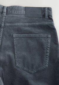 Dark blue corduroy pants feature vertical ribbing, a back pocket, and a leather patch on the waist with "DENIM SUPPLY" embossed.