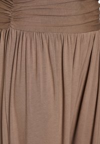 Brązowa, teksturowana tkanina z marszczeniami u góry i opadającymi fałdami poniżej, tworząca miękki spływ.