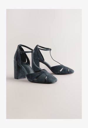 Dunkelblaue Wildleder-Pumps mit strukturierter Form, offenem Zehenbereich und Knöchelriemen; mit Cut-out-Akzenten an den Seiten.