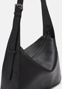 Borsa a spalla in pelle nera con una texture liscia e un design curvo. Presenta una tracolla regolabile e una chiusura con zip lungo la parte superiore.